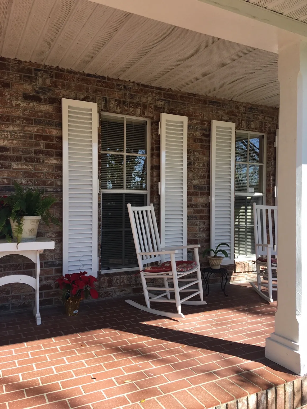 Brick porch with white rocking chairs, shutters, and potted plants