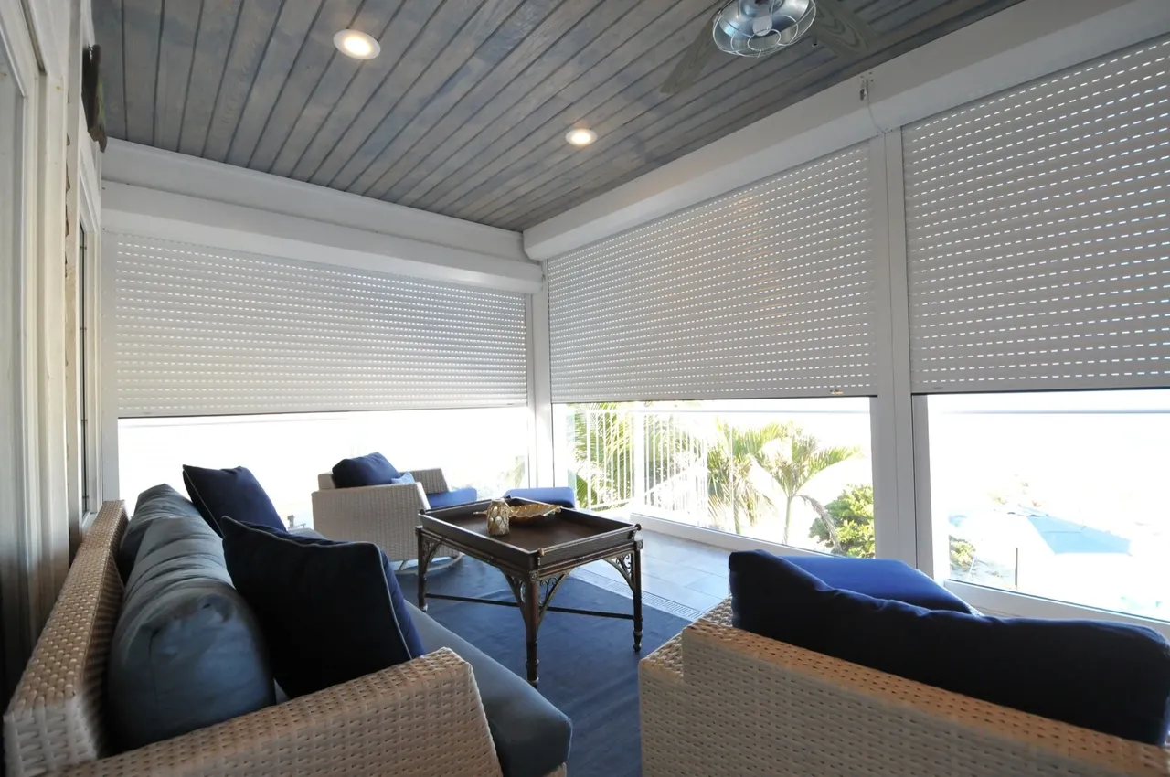Enclosed patio with blue cushions, white shutters, and ocean view